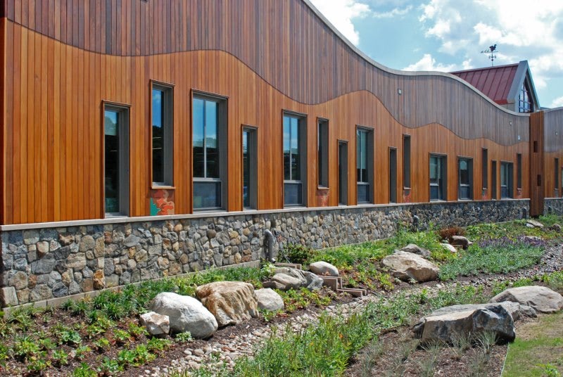 The vertical rainscreen siding curved front facade of the new Sandy Hook, CT School with lighter FSC Ipe wood on the bottom and darker FSC Machiche on the top, with a curved line flowing horizontally meet. 