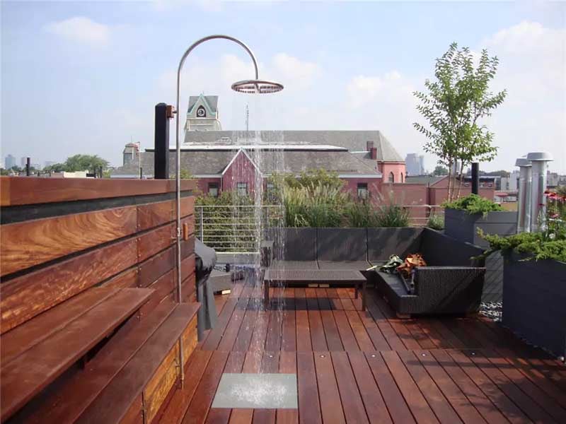 Ipe wood rooftop deck next to a pool area featuring an outdoor shower, built in benches and shelves, and privacy screen